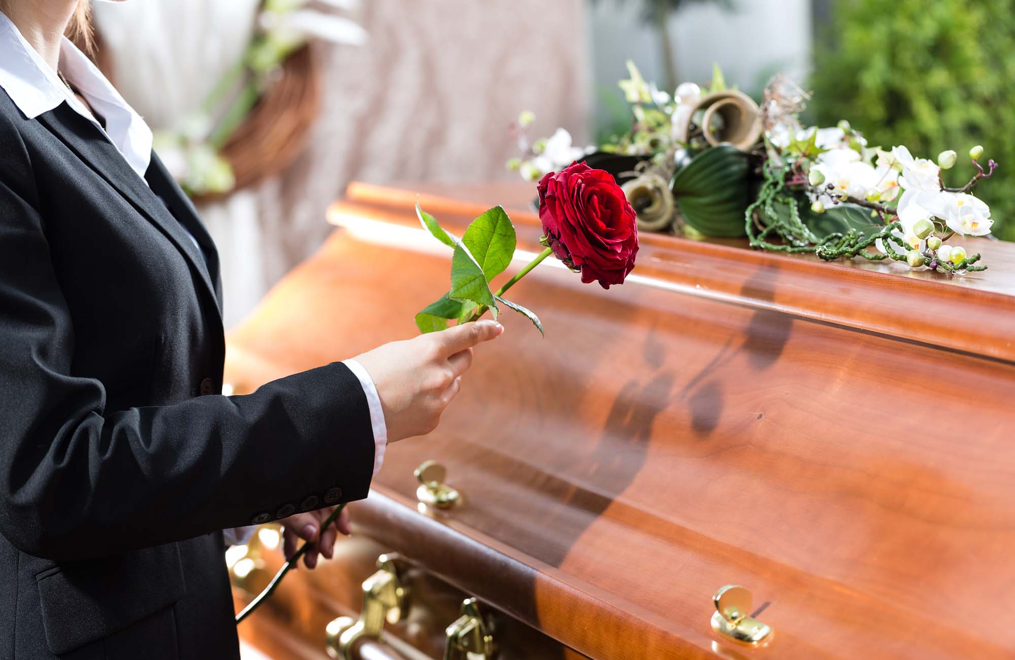 Woman holding a red rose beside a coffin in Falkirk