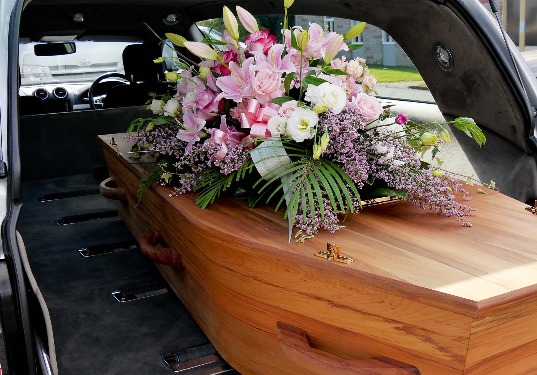 Oak coffin with pink and white flowers in the back of a hearse in Falkirk