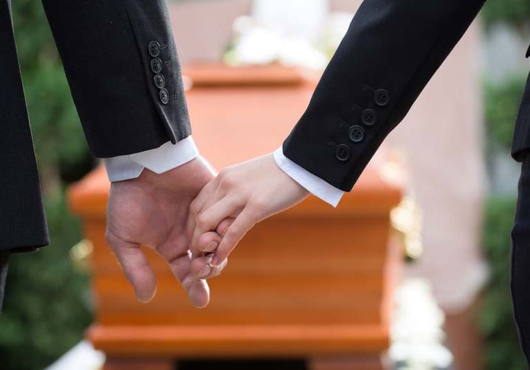 People at funeral consoling each other. Religion, death and dolor - couple at funeral holding hands consoling each other in view of the loss